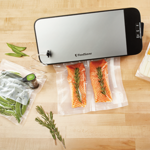 aparat de vidat metalic foodsaver pe masa de lemn cu fileuri de somon in punga